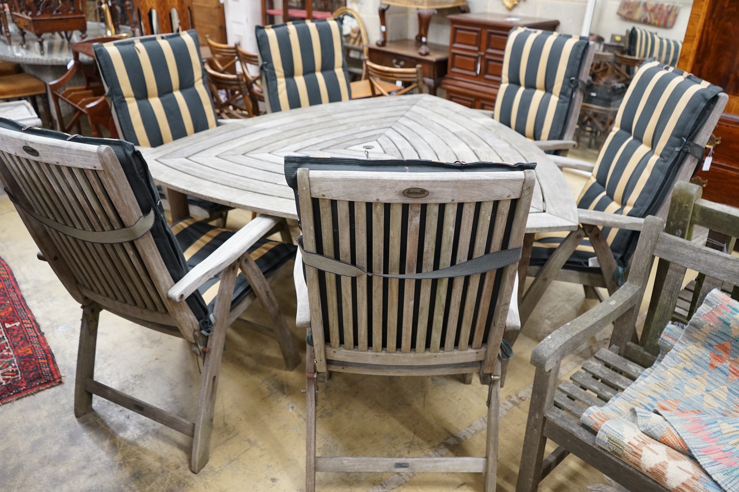 A Hartman weathered teak triangular garden table, width 170cm, height 76cm, six folding armchairs with seat pads and a tray top side table.